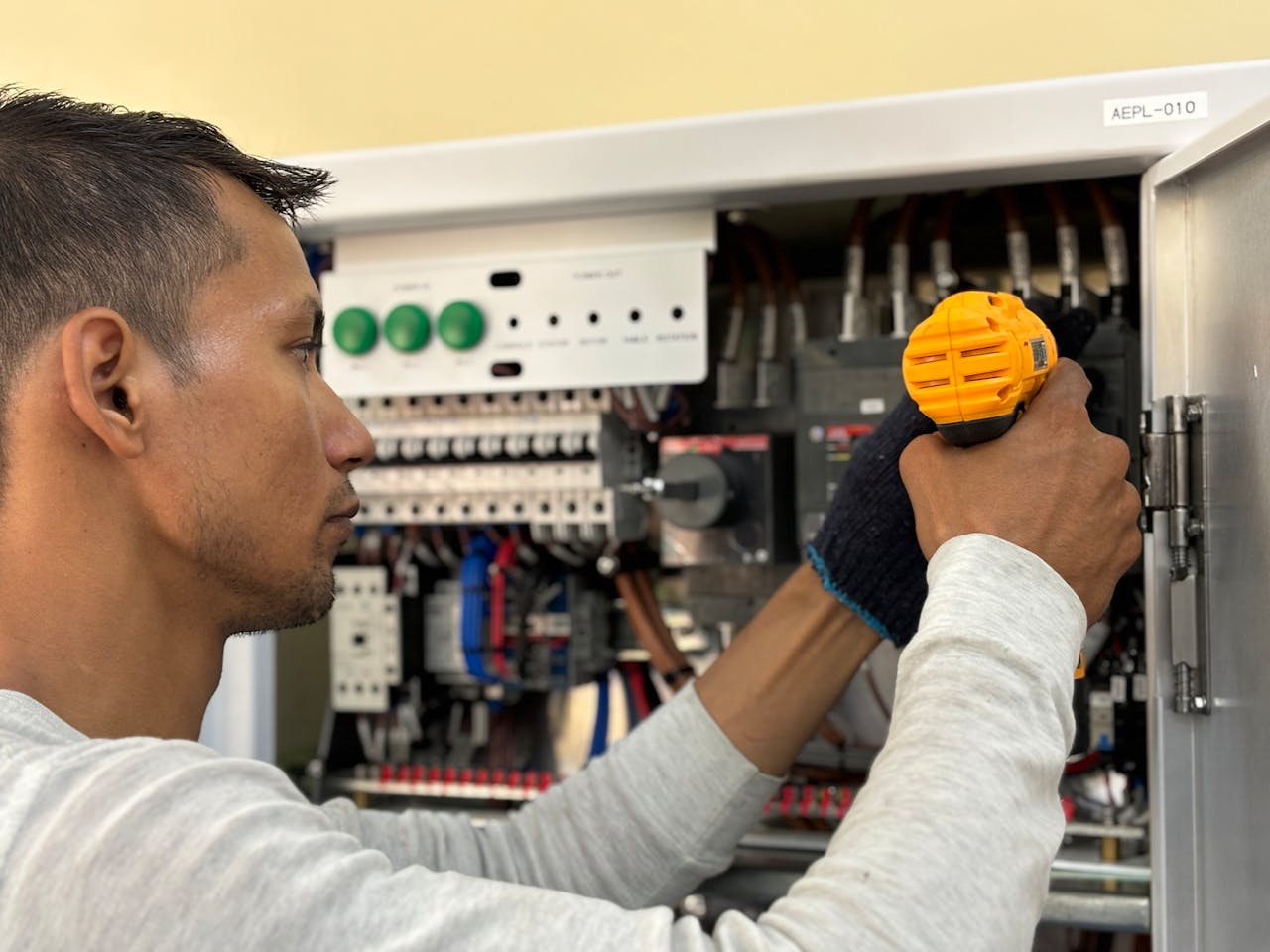 about-02 Skilled electrician using a drill to repair electrical equipment indoors. Focus on precision and safety.