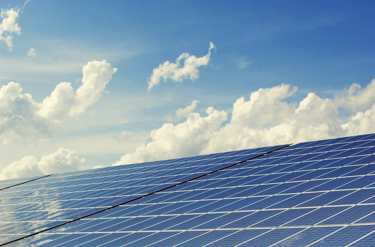impact-img Sleek modern solar panels under a vibrant blue sky with clouds, symbolizing clean energy.