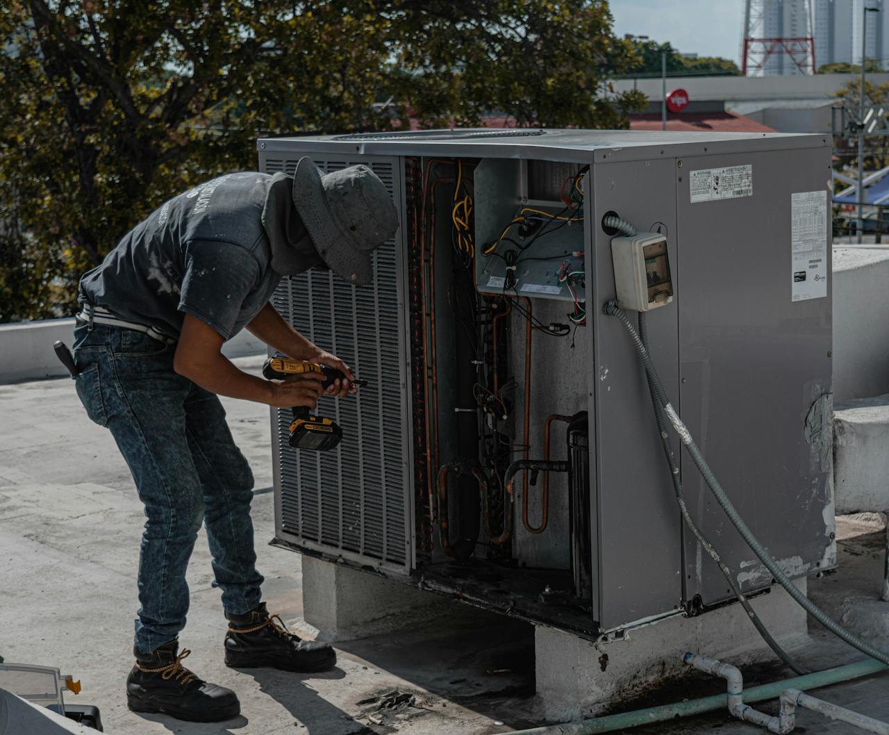 services-03 A worker in a bucket hat repairs an outdoor air conditioning unit on a rooftop.